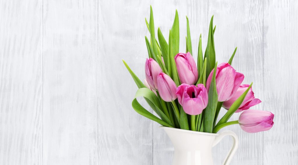 Fresh pink tulip flowers bouquet on shelf in front of wooden wall. View with copy space