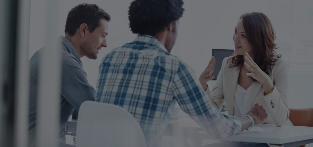Drei Personen sitzen an einem Bürotisch und beraten sich gemeinsam